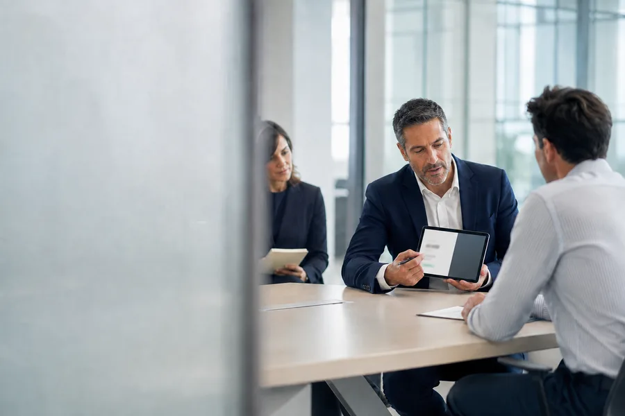 A consultant showing the proposal on a tablet to the customer opposite, while a colleague takes notes.